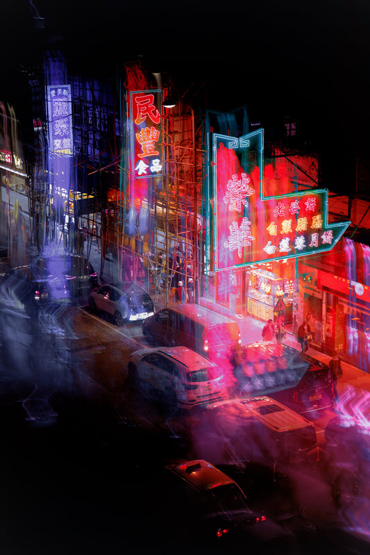 Vibrant long-exposure photograph of a neon-lit street at night, featuring colorful Chinese-style storefront signs in red, pink, blue, and green, with blurred cars and pedestrians creating a dynamic urban scene.