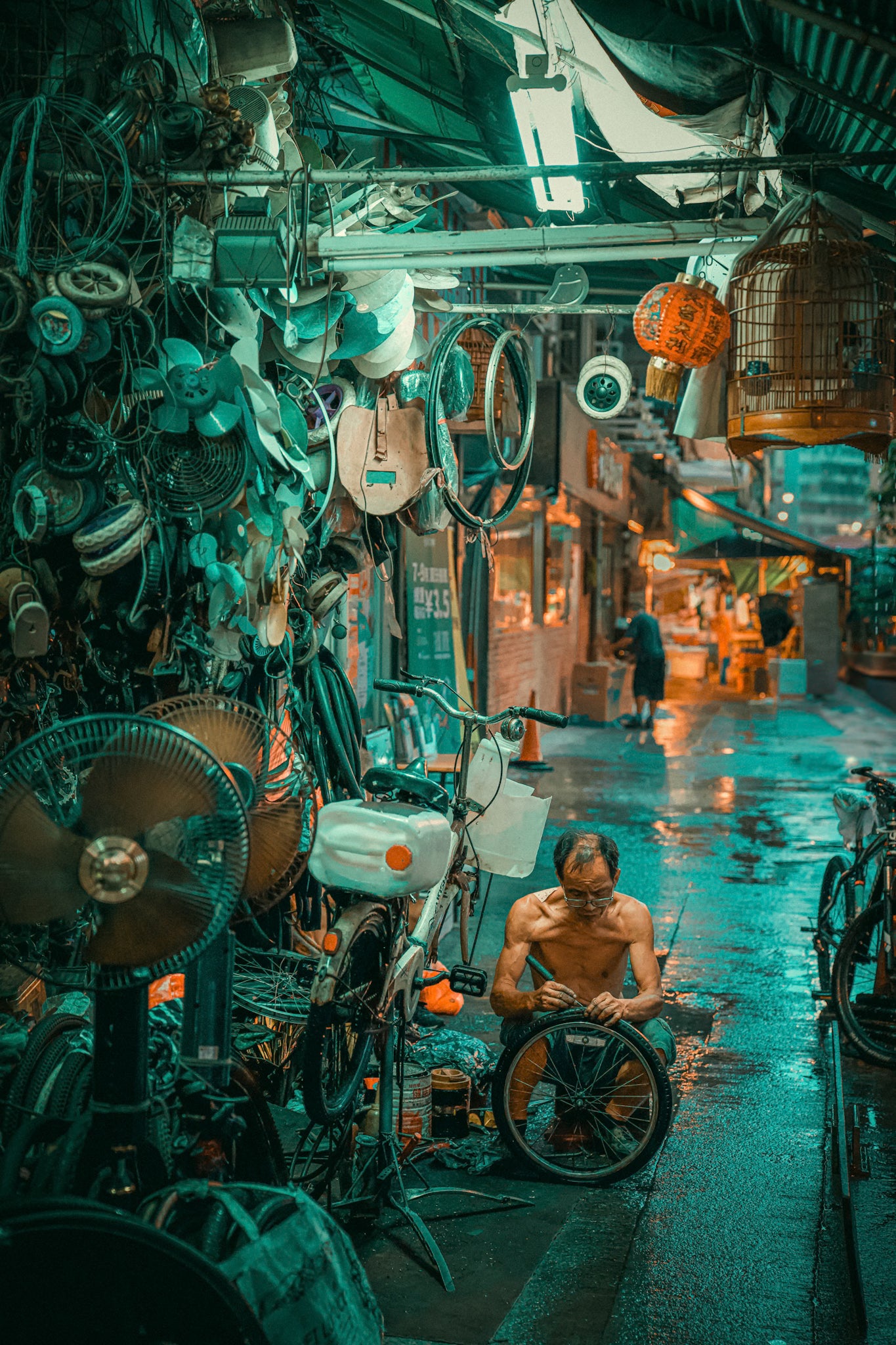 A person repairing a bicycle wheel in a cluttered indoor setting with various tools and parts around, under a teal hue.