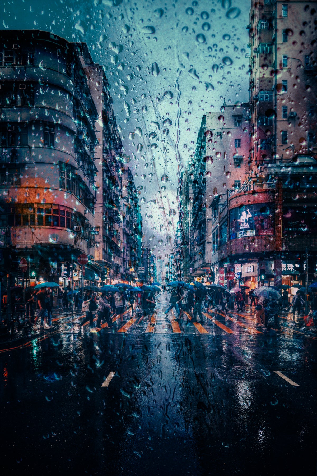 A rainy city street scene viewed through wet raindrops, with tall buildings on both sides, blurred pedestrians holding umbrellas, and blue-toned reflections on the wet pavement.