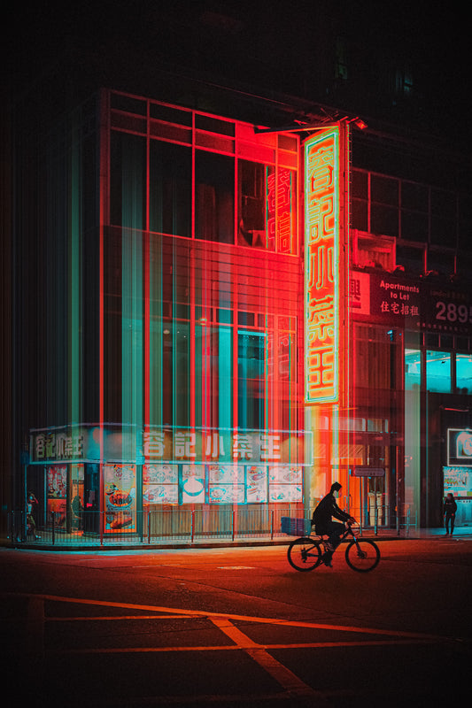 A person riding a bicycle on a street at night, with vibrant neon lights from surrounding buildings